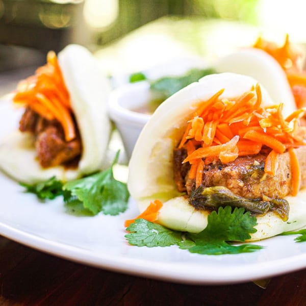 Three Vietnamese pork belly bao buns with pickled carrots and cilantro on a white plate.