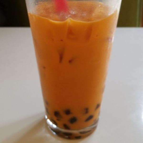 A tall glass of iced Vietnamese Thai tea with tapioca pearls and a pink straw.