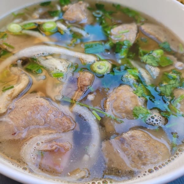 Close-up of a bowl of Vietnamese pho with beef, noodles, and fresh herbs in broth.