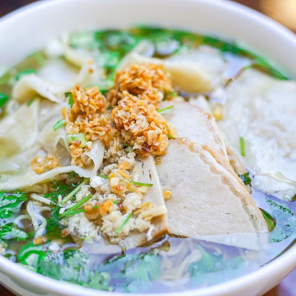 Close-up of a Vietnamese noodle soup with meat, herbs, and crispy fried garlic in a white bowl.