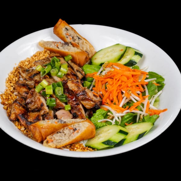 Vietnamese grilled chicken with spring rolls, fresh vegetables, and crushed peanuts on a white plate.