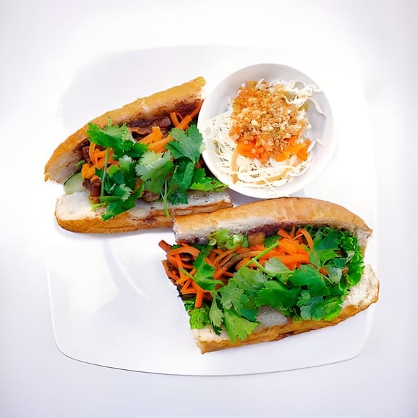 Two Vietnamese banh mi sandwiches with cilantro, carrots, and meat, served with a side salad.